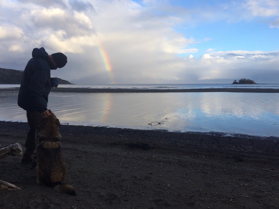 Photograph of a hiker under a rainbow, petting a dog